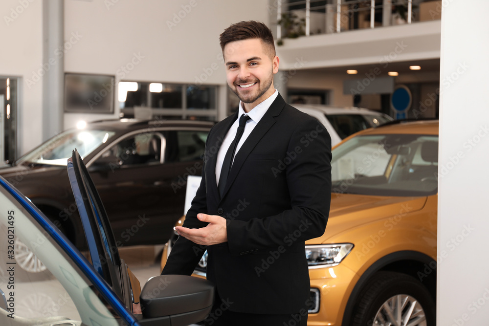 Young salesman near new car in dealership