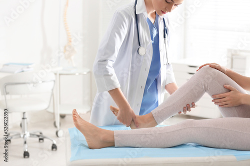 Female orthopedist examining patient's leg in clinic, closeup photo