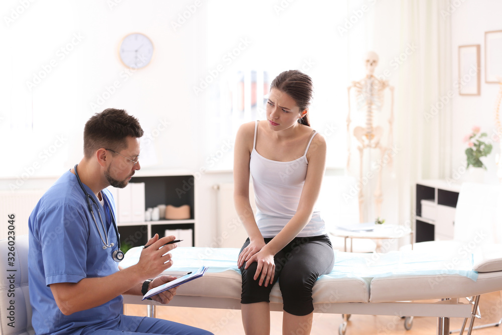 Male orthopedist examining patient with injured leg in clinic Male orthopedist examining patient with injured leg in clinic