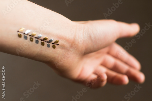 hand of a young woman wih gold floral leaves temporary tattoo on her wrist