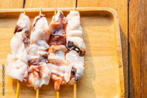 Fresh cut squid on skewers in a wooden tray on a wooden table