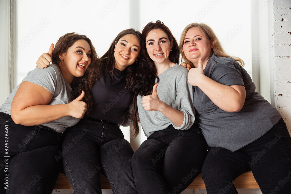 Young caucasian women in casual clothes having fun together. Friends sitting near by window and laughting, spending time together. Bodypositive, nutrition, feminism, loving themself, beauty concept. Young caucasian women in casual clothes having fun together. Friends sitting near by window and laughting, spending time together. Bodypositive, nutrition, feminism, loving themself, beauty concept.