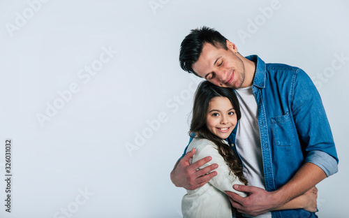 The best feeling. Close-up photo of a young proud dad, who is hugging his cute little daughter with his eyes closed, while they are both smiling. photo