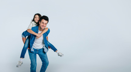 The best dad ever. Full-length photo of a little girl and her dad having fun together, while a child is riding on her father’s back and hugging him, both are smiling and looking in the camera.