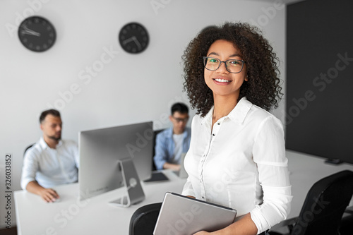 Smiling woman looking at camera in office with colleagues