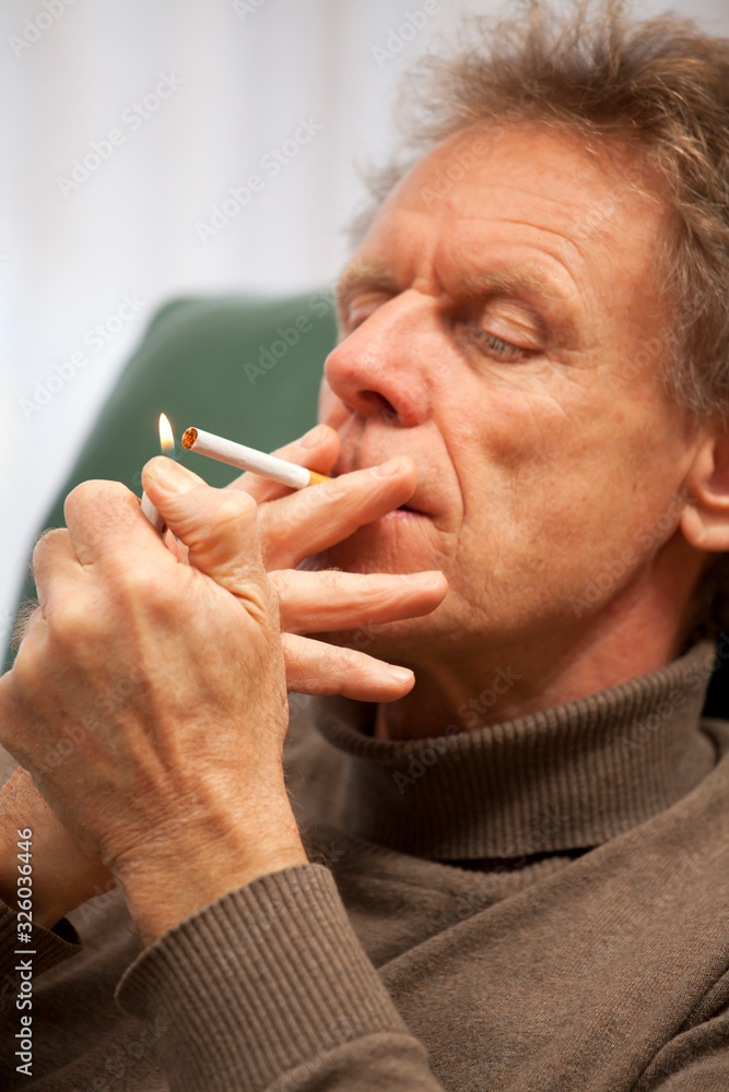 Attractive mature man lights a cigarette while sitting in a chair in a living room Attractive mature man lights a cigarette while sitting in a chair in a living room
