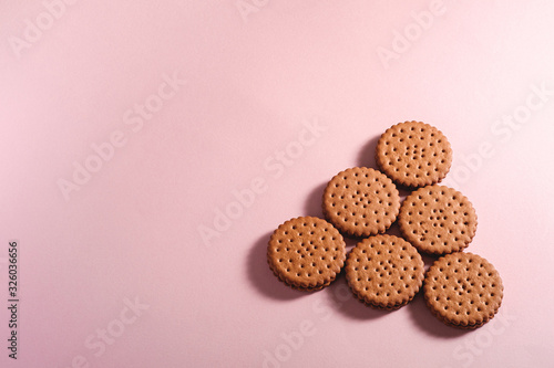 Chocolate sandwich cookie with cream, sweet food from store, on pink pastel background, angle view