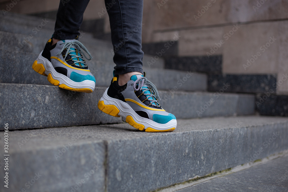 Feet  shod in sneakers multi-colored yellow, white, black and blue down the marble stairs