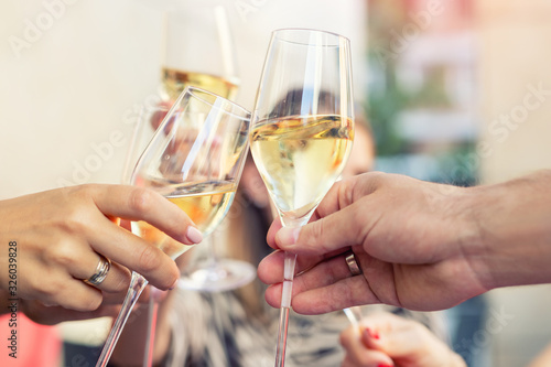 Close-up detail of men and woman hands clinking glasses of white champagne or prosecco at party or celebration event outdoors. People having fun enjoy drink alcohol toasting cheers at cafe restaurant photo