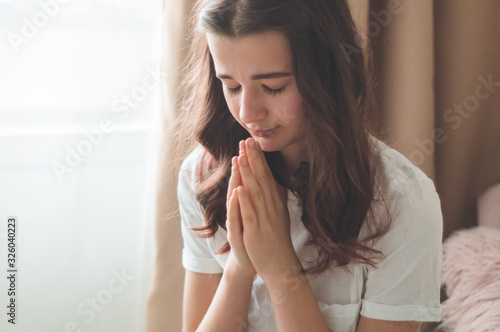 Teenager Girl closed her eyes  praying in a in the living room. Hands folded in prayer concept for faith  spirituality and religion. Peace  hope  dreams concept