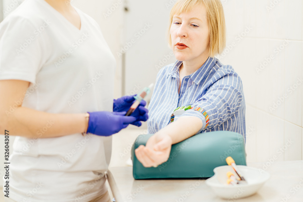 Fototapeta premium Pensive man is sitting in clinic. Female doctor is doing blood test
