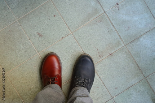 Closeup upper of mismatched shoes, a man wearing two different shoes and different colors standing on tiled floor, break the rules, revolution metaphor 