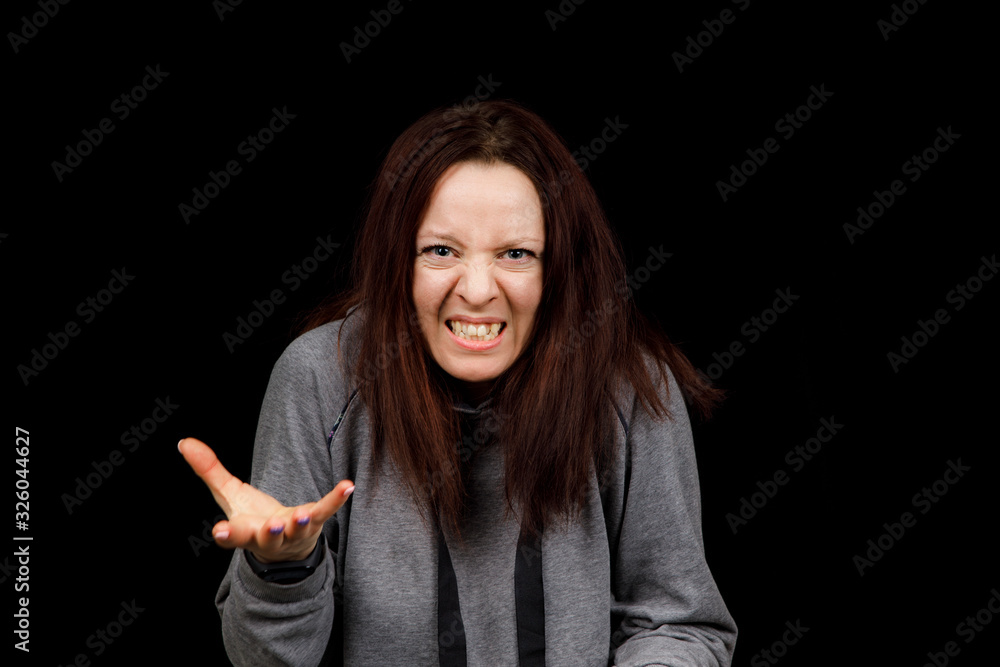Middle age woman is angry. The girl wear casual sweeter on a black background. Evil woman, hands on her sides Middle age woman is angry. The girl wear casual sweeter on a black background. Evil woman, hands on her sides