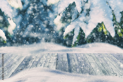 Snowing on Weathered Wooden Desk for Product Display on Winter Background with Spruce Branches Covered with Snow on Forest on Blurred Background © handatko