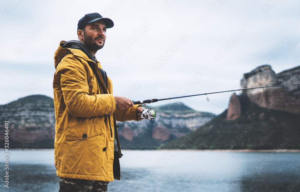 beard fisherman hold in hand fishing rod, man enjoy hobby sport on mountain  river, person catch fish on background nature blue sky, fishery concept  Stock Photo