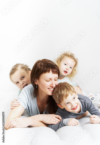 Family time: Mom and three children lie on a white bed, hugging and laughing cheerfully.