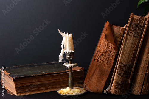 Stack of ancient books with yellowed shabby pages and bronze candlestick with candle