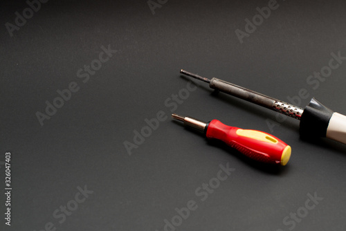 electric soldering iron and screwdriver on a black background