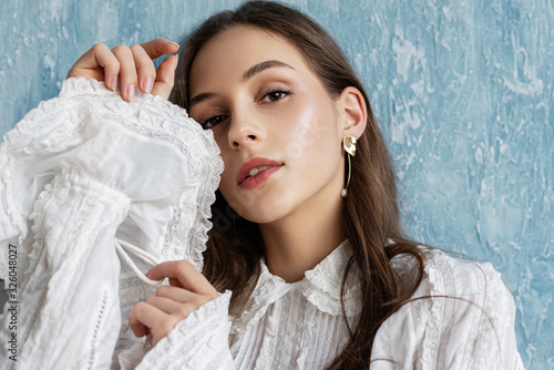Photographie Close up portrait of beautiful fashionable woman with natural flawless skin, wearing trendy vintage style white blouse, pearl earrings