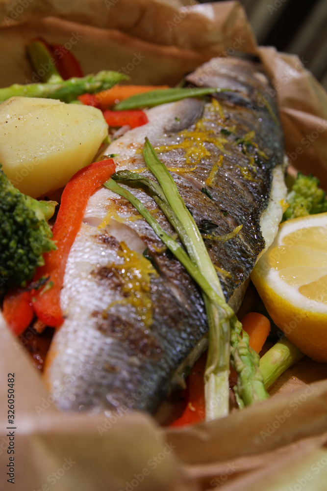 Grilled seabass with vegetables and lemon.Served on paper.Close up Grilled seabass with vegetables and lemon.Served on paper.Close up