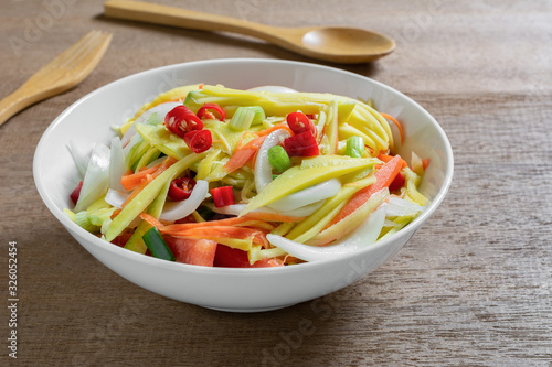 close up of spicy mango salad in a ceramic bowl on wooden table. asian homemade style food concept.