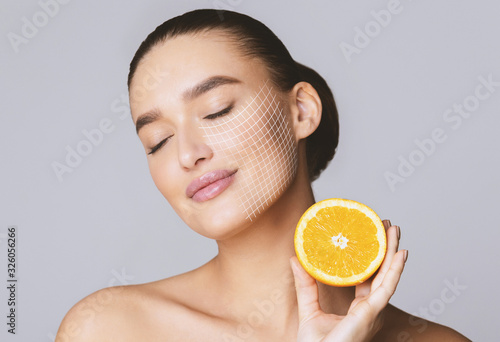 Delighted young pretty woman with closed eyes holding orange half photo