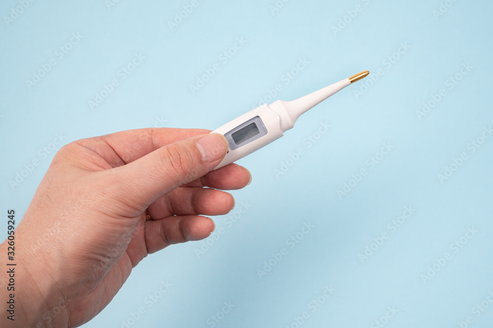 A male hand holding a digital thermometer in hand on a blue background. A male hand holding a digital thermometer in hand on a blue background.