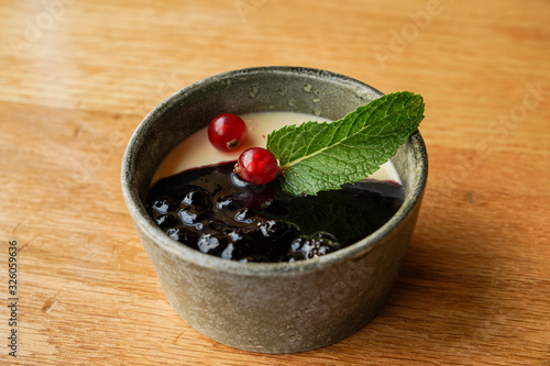 Panna cotta dessert in ramekin round with fresh cranberry and blueberry jam garnish with mint leaf on the wooden table