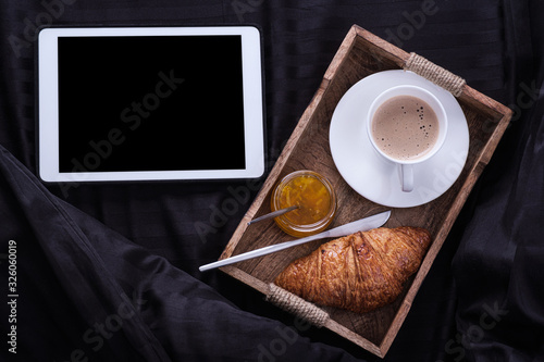 Breakfast in bed - tablet pc with coffee and croissants and jam