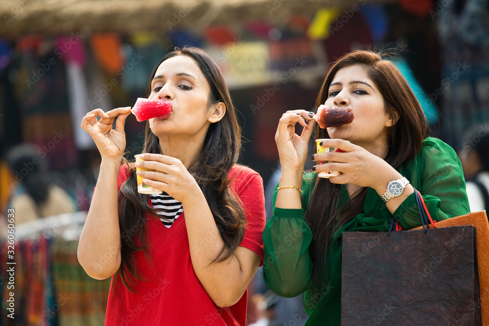Two women eating flavored ice gola dipped in syrup Two women eating flavored ice gola dipped in syrup