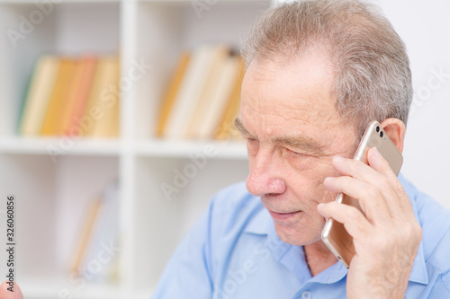 Elderly man talking on a cell phone on the background of shelving with books