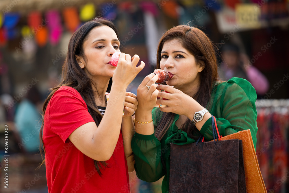 Two women eating flavored ice gola dipped in syrup Two women eating flavored ice gola dipped in syrup