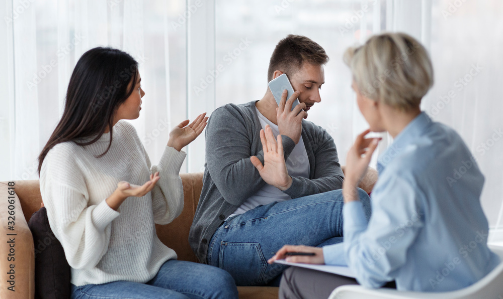 Wife Blaming Husband, He Talking On Cellphone In Counselor's Office Wife Blaming Husband, He Talking On Cellphone In Counselor's Office