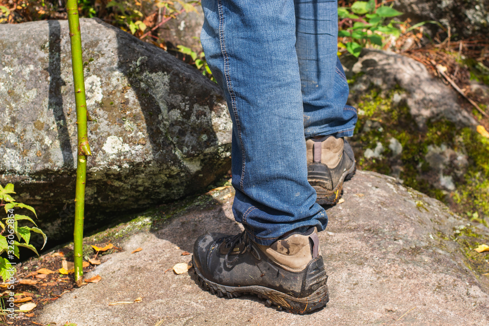 Legs of a tourist in hiking boots on a walk along a mountain trail. A man in black boots and blue jeans against the backdrop of mountain boulders. The concept of relaxation and adventure.