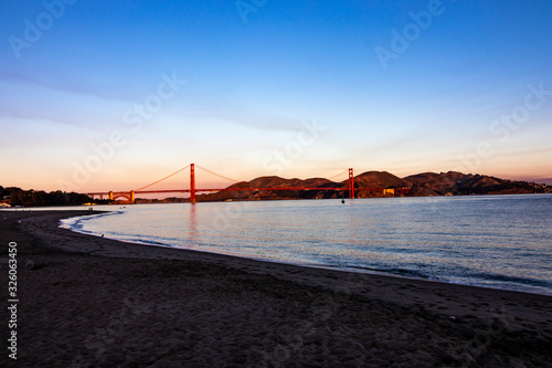 Sunset over San Francisco Bay, California with the red Golden Gate Bridge and mountains in the background and wave and light reflecting in the water in the foreground, horizontal image
