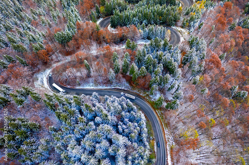 Aerial view of a winding mountain road passing through a fir trees forest. Winter with snow