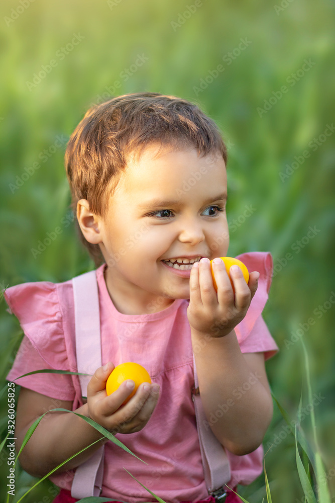 Girl holding easter eggs in her hands on a background of green grass. Kid wants to eat an egg. Funny toddler with yellow eggs, happy easter Girl holding easter eggs in her hands on a background of green grass. Kid wants to eat an egg. Funny toddler with yellow eggs, happy easter