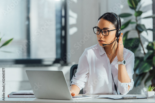 asian translator working online with headset and laptop in office photo