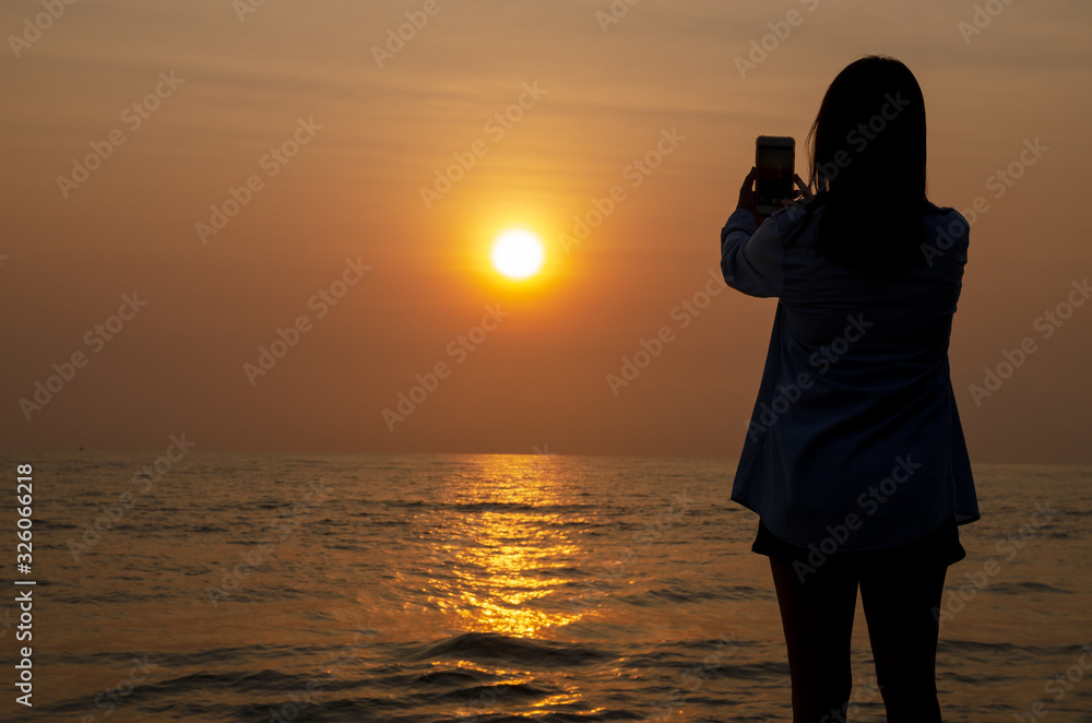silhouette of woman take photo sunset on the sea and colorful sky by smartphone.