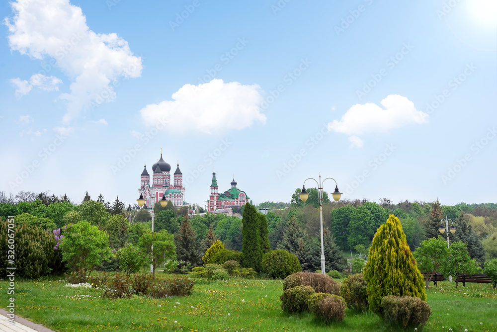 Public park landscape with view of big Church and decorative trees composition on a blue sky background.