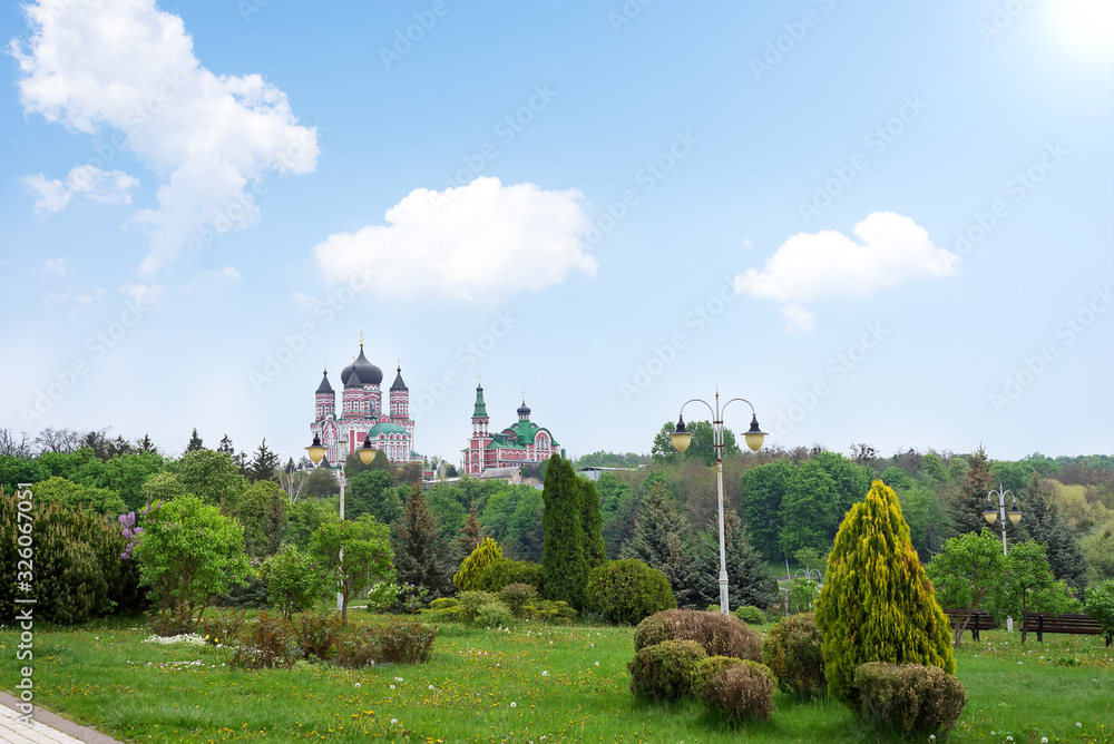 Naklejka premium Public park landscape with view of big Church and decorative trees composition on a blue sky background.