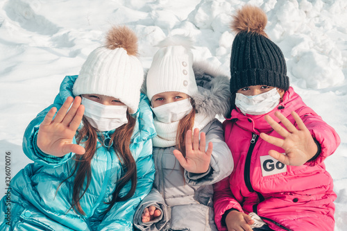 Three teenage girls in protective masks are sitting on the snow in the park. Girls show a gesture of denial. Stop the epidemic of viruses and flu. Stop coronovirus photo