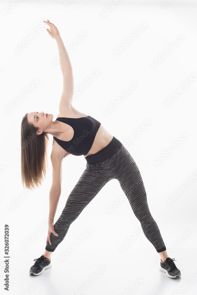 Portrait of sporty fit beautiful young brunette woman in sportswear bra and black pants working out, doing Utthita Trikonasana, Extended Triangle pose, studio full length, isolated, white background