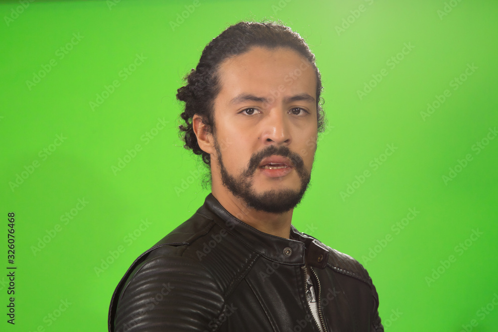 Obraz premium portrait of attractive Latin young in rocker jacket, on green background, with acoustic guitar