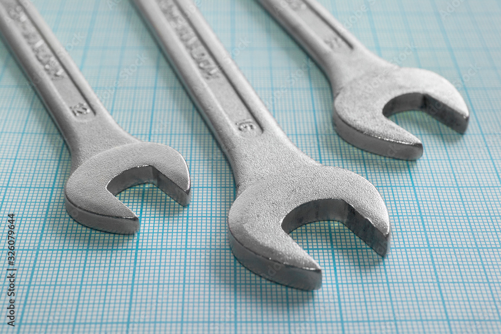 Close-up of three gray steel wrenches on blue graph paper. Close-up of three gray steel wrenches on blue graph paper.