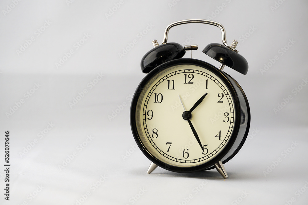 Classic black round alarm clock on a white background. Lunch time at office concept. A nice addition to the modern interior of any home or office. Classic black round alarm clock on a white background. Lunch time at office concept. A nice addition to the modern interior of any home or office.