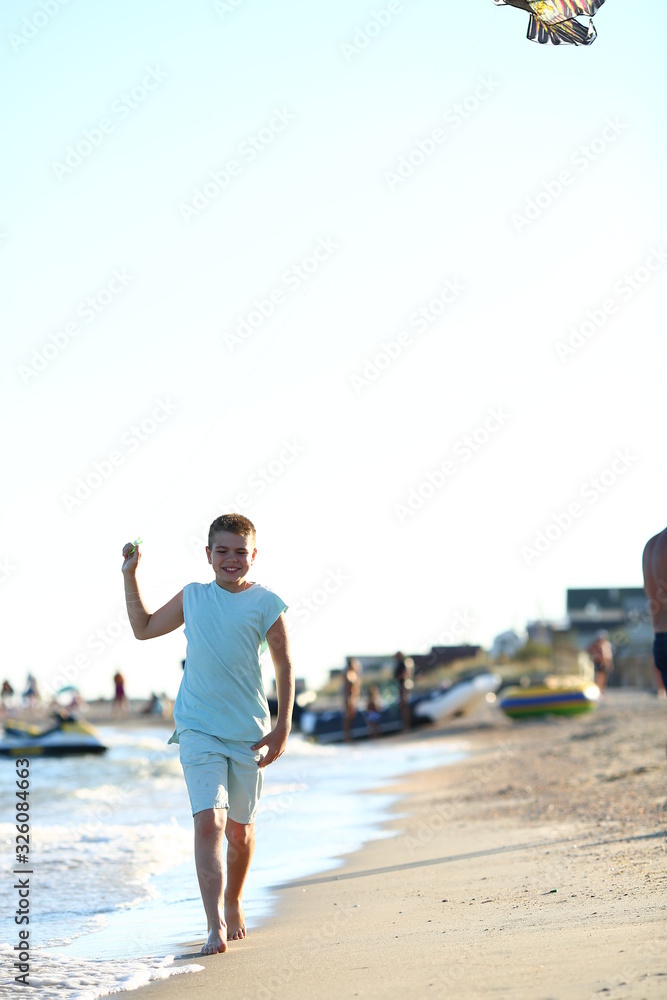  handsome boy in shorts and a t-shirt teenager launches a kite on the sky on the seashore in summer