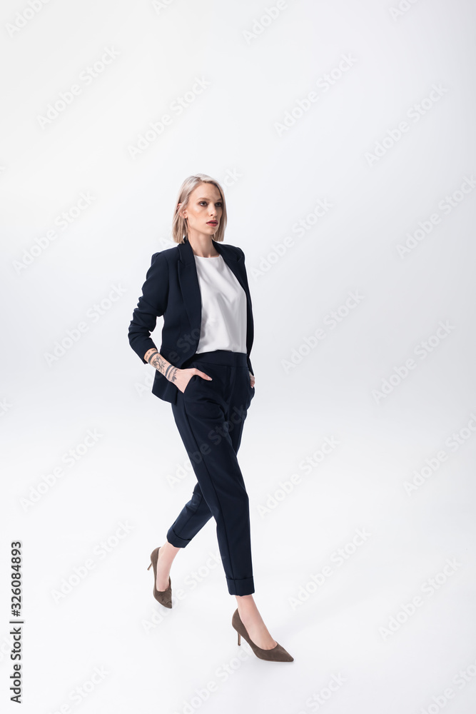 successful young tattooed businesswoman walking with hands in pockets on white