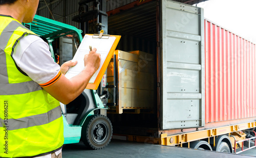 Worker Holds a Clipboard Controlling the Loading of Packaging Boxes into Shipping containers. Supply Chain. Forklift Tractor Trucks Loading at Dock Warehouse. Cargo Shipment. 