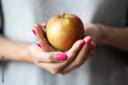 Female hands with perfect pink manicure hold an apple, concept photo